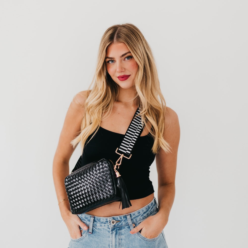 Black woven camera crossbody bag with white check pattern, tassel, and gold hardware