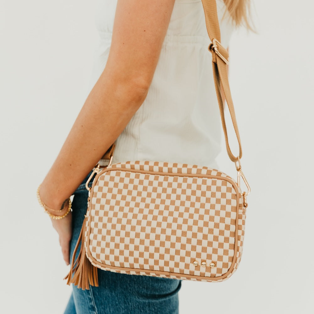 Woven checkered camera crossbody bag in tan and brown with tassel fringe and wristlet-style strap.