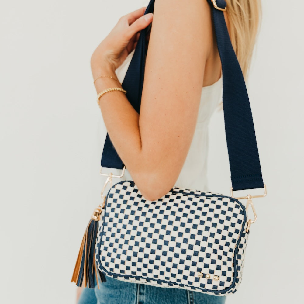 Woven checkered camera crossbody bag in navy and white with tassel fringe detail.