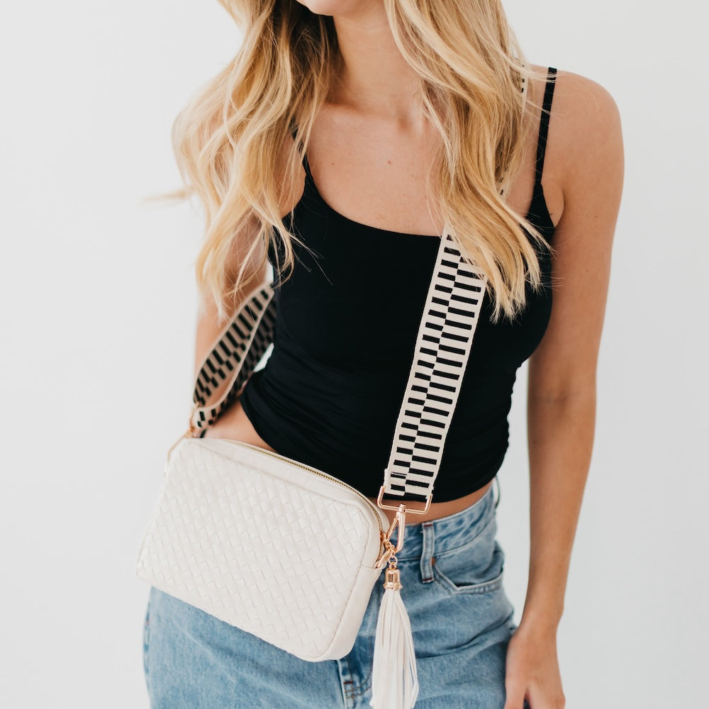 Cream woven camera crossbody bag with tassel and black-and-white striped strap