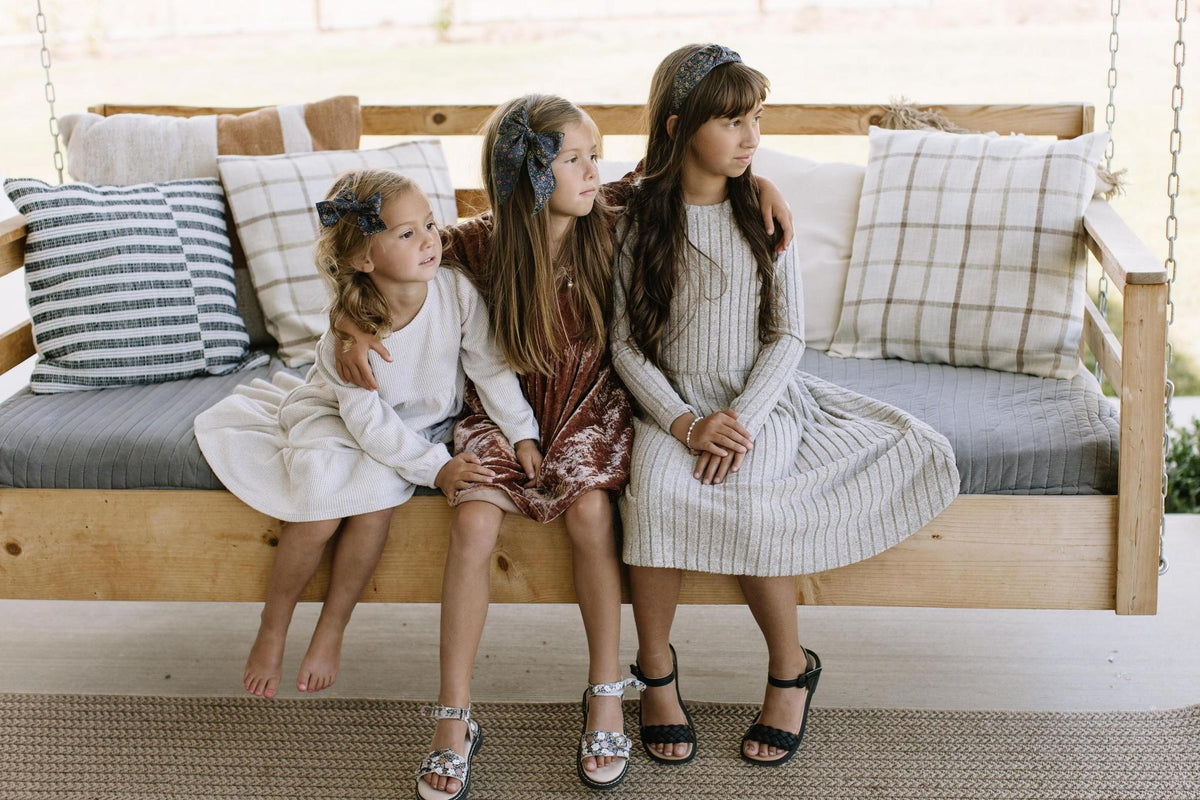Children seated on a sofa wearing dark green floral hair bows
